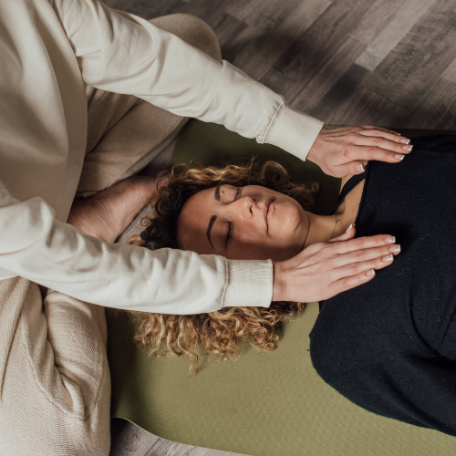 Person lying on a mat receiving a reiki session, with hands hovering over their chest.