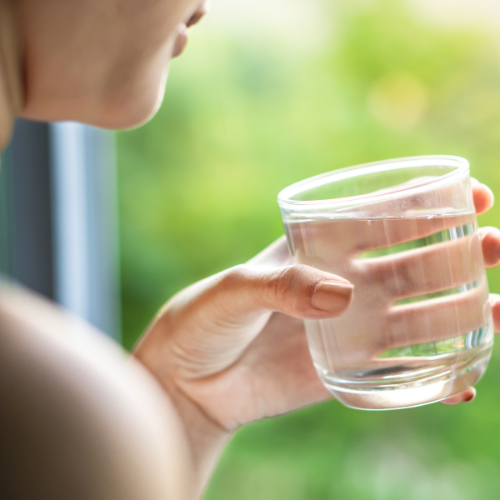 Person holding a glass of water in front of a green, blurred background.