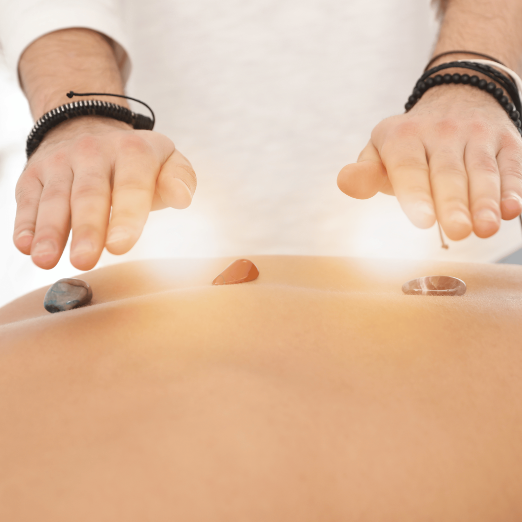 A person holds their hands above a back with three reiki crystals placed on it, appearing to practice an energy healing journey.