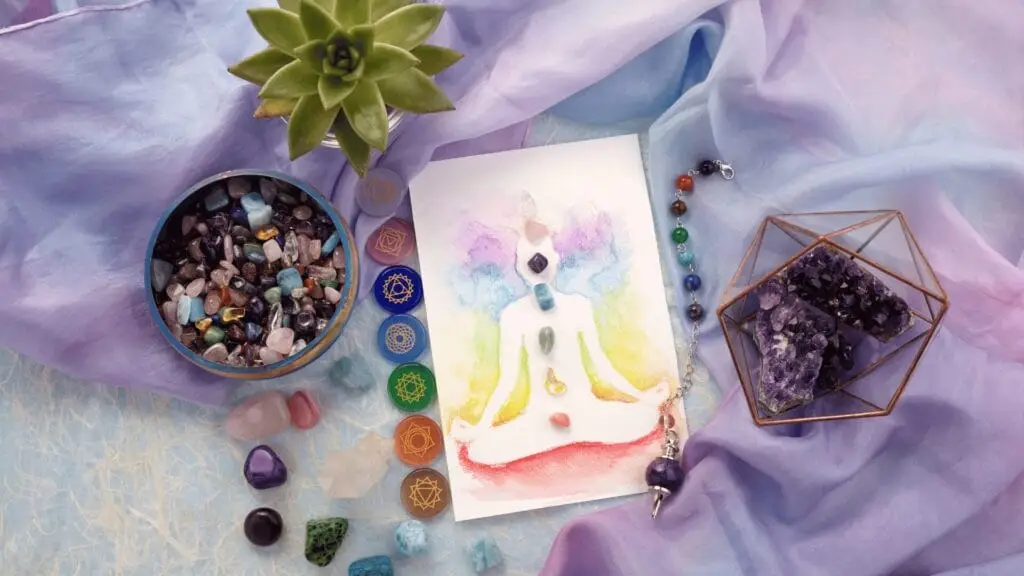 A watercolor painting of a meditating figure with chakras, surrounded by enhancing Reiki crystals, a succulent, and chakra symbols on a purple and blue cloth.