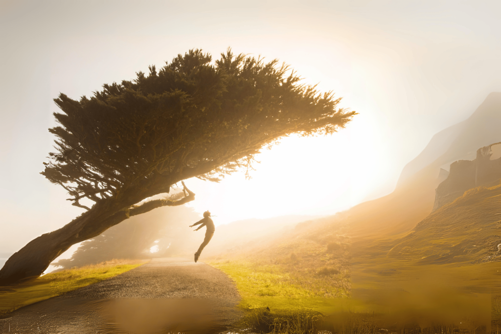 The Future of Reiki in Mental Health Care A person leaping with joy near a wind-swept tree on a sunlit path, embracing the energy balance, as a foggy hillside looms in the background.