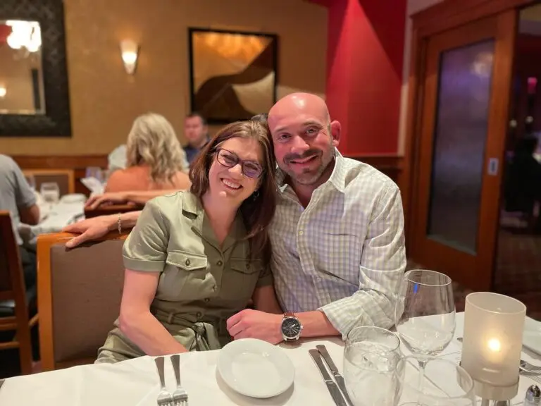 A smiling couple sits together at a restaurant table, with dinnerware and glasses in front of them, as vibrant abstract artwork energizes the walls around them.