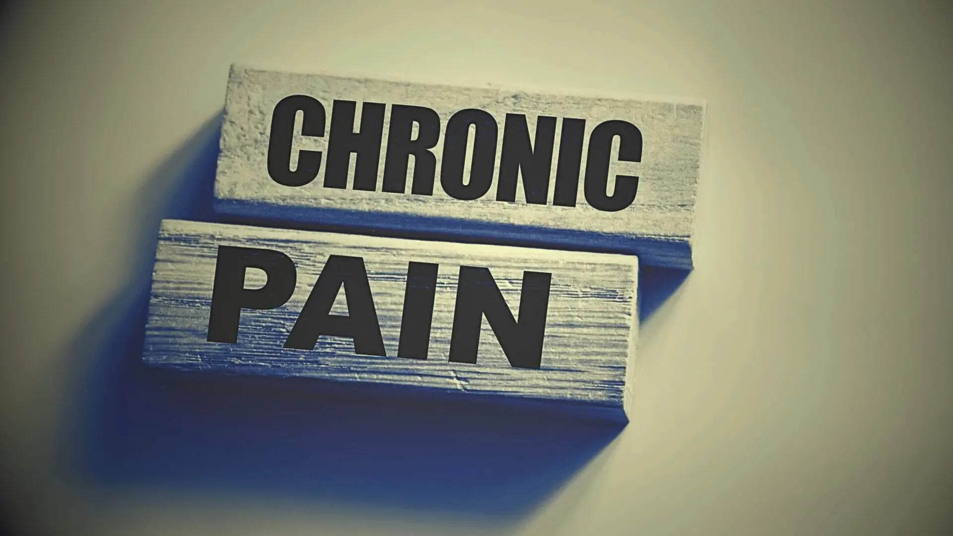 Two wooden blocks display the words "CHRONIC PAIN" in bold black letters against a plain background, symbolizing the importance of Chronic Pain Management for improved well-being.