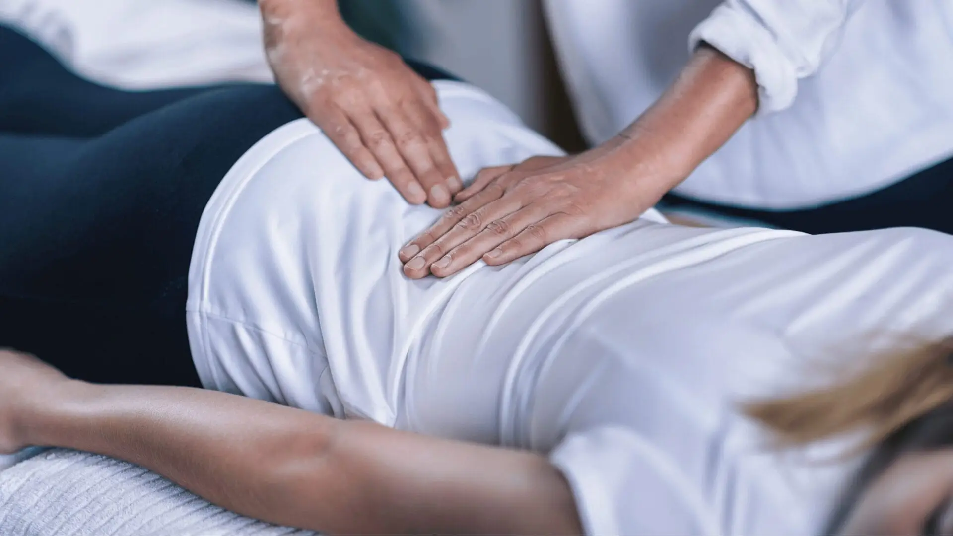 A person lying face down receives a massage, with hands pressing on their lower back, incorporating Reiki therapy for enhanced benefits in chronic pain management.