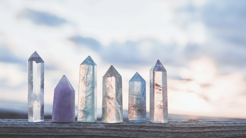 Six pointed Reiki crystals of varying sizes and colors are lined up on a wooden surface, set against a cloudy sky backdrop, inviting you to begin your healing journey.
